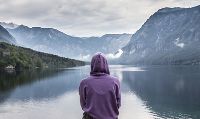 Image showing Woman wearing purple hoodie watching tranquil overcast morning scene at lake Bohinj, Alps mountains, Slovenia.