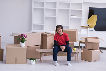 Image showing boy sitting on the table with cardboard boxes around him