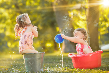 Image showing The cute little blond girls playing with water splashes on the field in summer