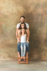 Image showing Pregnant mother with teen daughter and husband. Family studio portrait over brown background