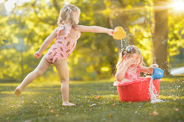 Image showing The cute little blond girls playing with water splashes on the field in summer