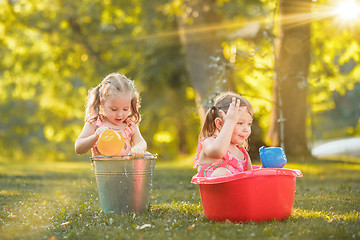 Image showing The cute little blond girls playing with water splashes on the field in summer