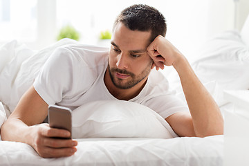 Image showing young man with smartphone in bed in morning