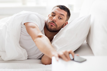 Image showing young man reaching for smartphone in bed