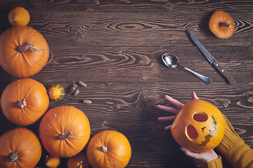 Image showing Hands holding Halloween pumpkin over wooden background