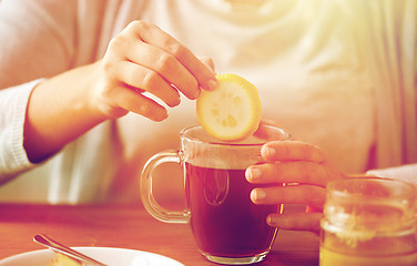 Image showing close up of woman adding lemon to tea with honey