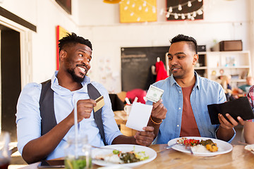 Image showing happy friends with money paying bill at restaurant