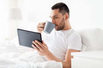 Image showing man with tablet pc drinking coffee in bed at home
