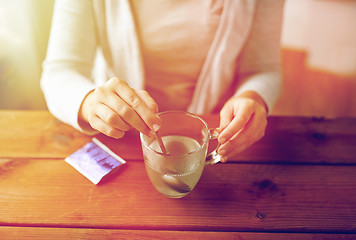 Image showing woman stirring medication in cup with spoon