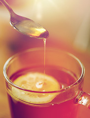 Image showing close up of woman adding honey to tea with lemon