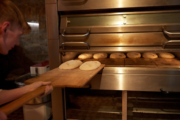 Image showing baker putting dough into bread oven at bakery