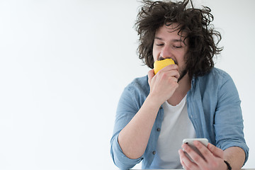 Image showing young man eating apple and using a mobile phone  at home