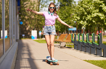 Image showing happy teenage girl in shades riding on longboard