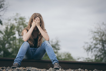 Image showing Portrait of young sad ten girl sitting outdoors at the day time.