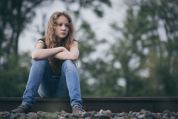 Image showing Portrait of young sad ten girl sitting outdoors at the day time.