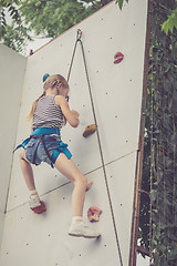 Image showing little girl climbing a rock wall outdoor.