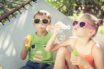 Image showing Two happy children lie on a hammock and play with soap bubbles