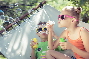 Image showing Two happy children lie on a hammock and play with soap bubbles