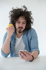 Image showing young man eating apple and using a mobile phone  at home