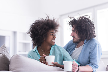 Image showing multiethnic couple sitting on sofa at home drinking coffe