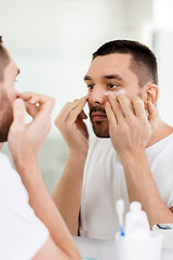 Image showing young man applying cream to face at bathroom