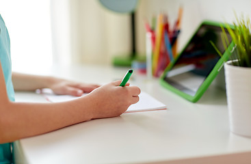 Image showing girl with tablet pc writing to notebook at home