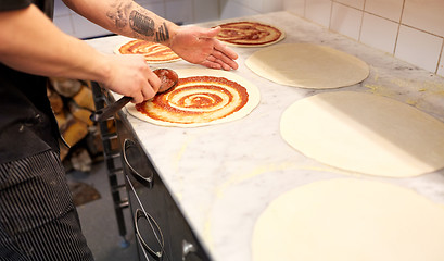 Image showing cook applying tomato sauce to pizza at pizzeria