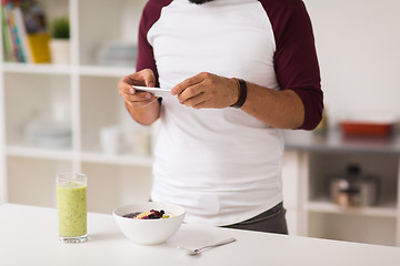 Image showing man with smartphone having breakfast at home