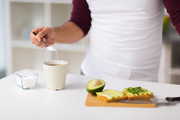 Image showing man having breakfast and adding sugar to coffee