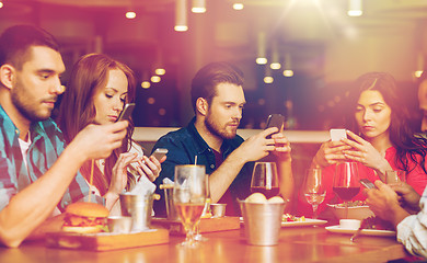 Image showing friends with smartphones dining at restaurant