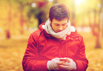 Image showing young man with smartphone walking at autumn park