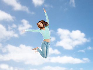 Image showing smiling young woman jumping in air over blue sky