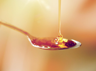 Image showing close up of honey pouring to teaspoon