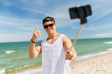 Image showing man with smartphone selfie stick on summer beach