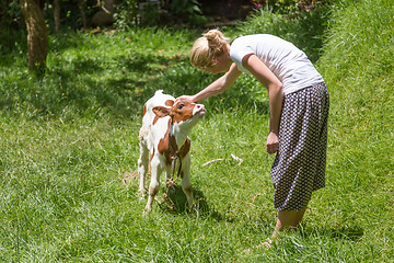 Image showing Woman caressing cute baby cow on meadow.