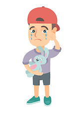 Image showing Caucasian boy in a cap crying and holding toy.