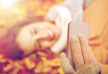 Image showing woman on autumn leaves taking selfie by smartphone