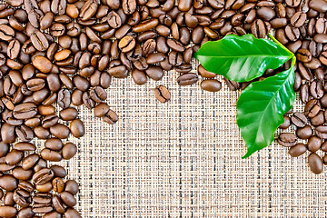 Image showing Coffee black grains with leaf on brown woven fabric