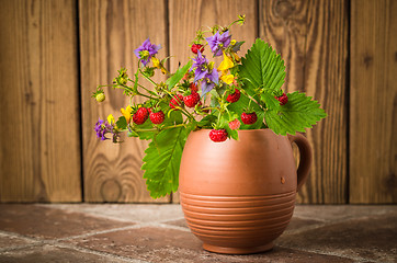 Image showing Ripe strawberries and a bouquet of forest flowers in a clay mug