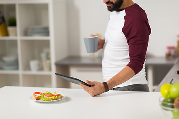Image showing man with tablet pc eating at home kitchen