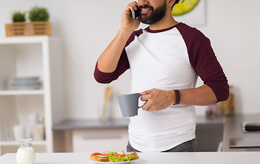 Image showing man calling on smartphone and eating at home