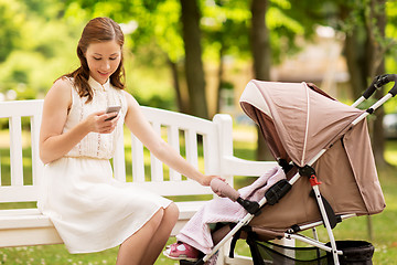 Image showing happy mother with smartphone and stroller at park