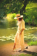 Image showing beautiful european woman in a white dress and in a hat dips her 