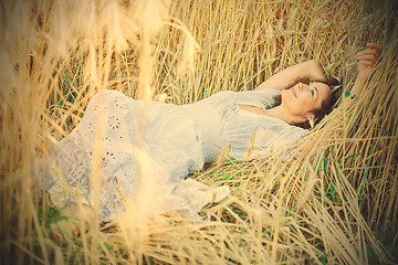 Image showing beautiful woman in a white dress lies in the ears of corn