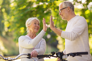 Image showing senior couple with bikes making high five at park