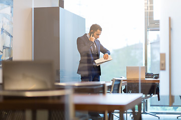 Image showing Businessman talking on mobile phone while looking at wristwatch.