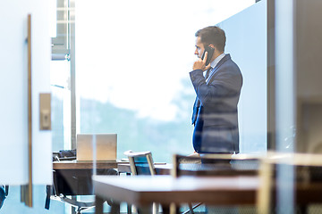 Image showing Businessman talking on a mobile phone while looking through window.