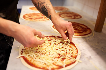 Image showing cook adding grated cheese to pizza at pizzeria