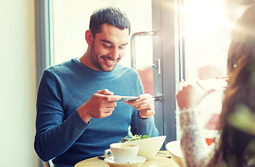 Image showing happy couple picturing food by smartphone at cafe