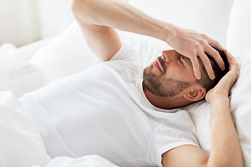 Image showing man in bed at home suffering from headache